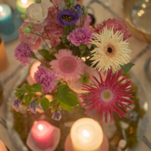 A floral arrangement featuring pink and purple flowers surrounded by lit candles on a table.