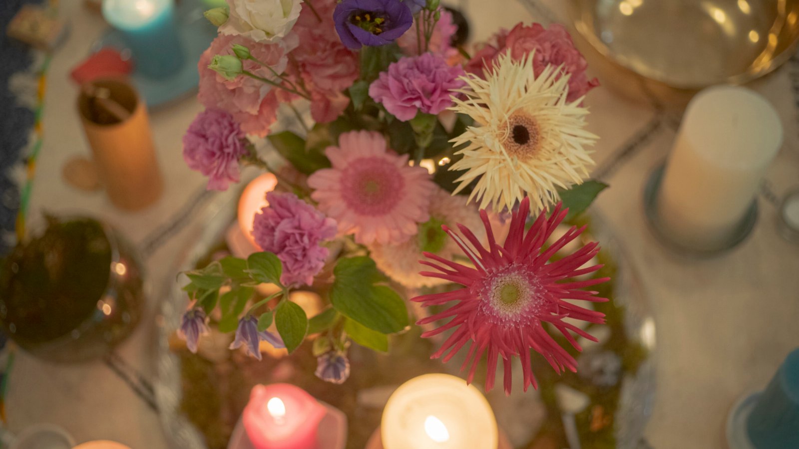 A floral arrangement featuring pink and purple flowers surrounded by lit candles on a table.