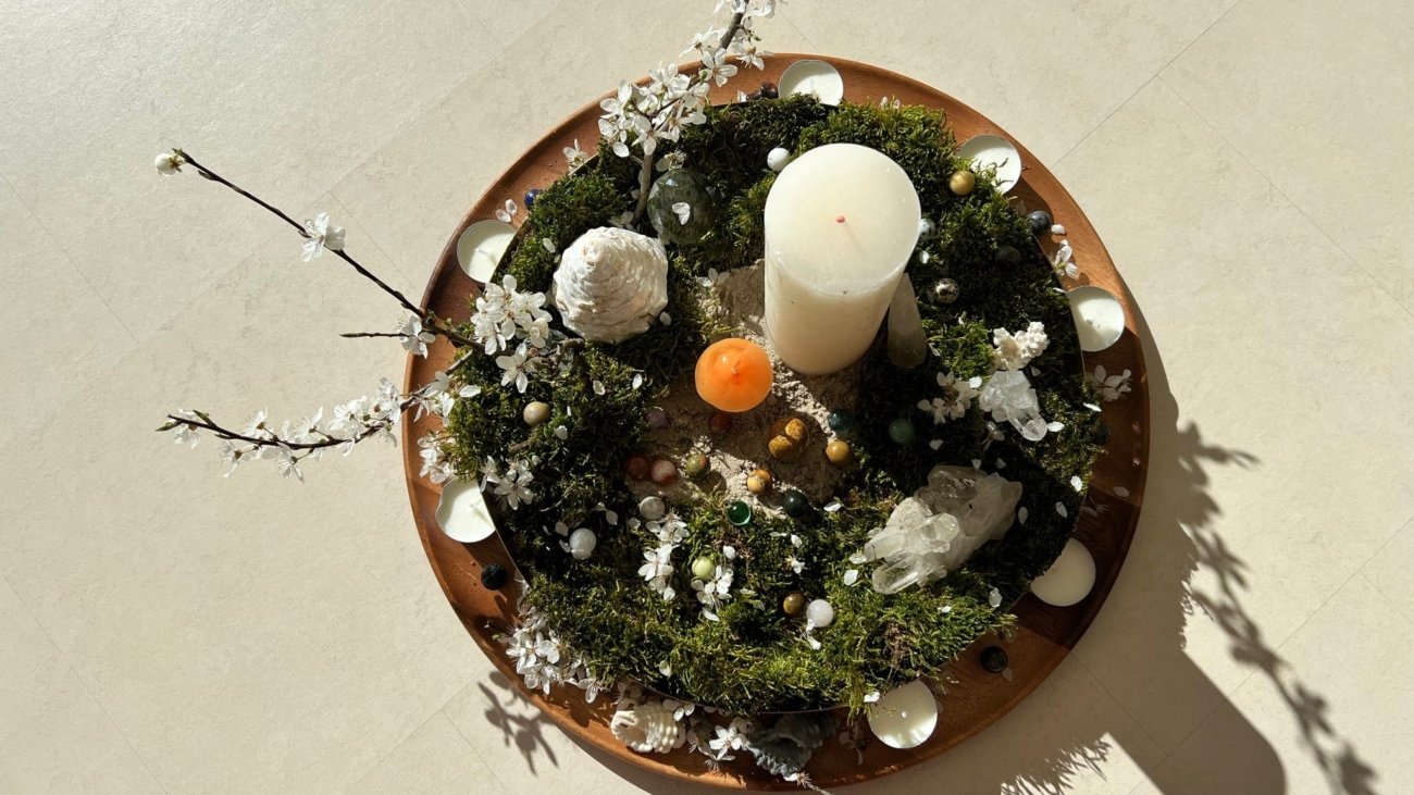 Centro de mesa redondo con musgo, velas, flores y piedras decorativas en una base de madera.