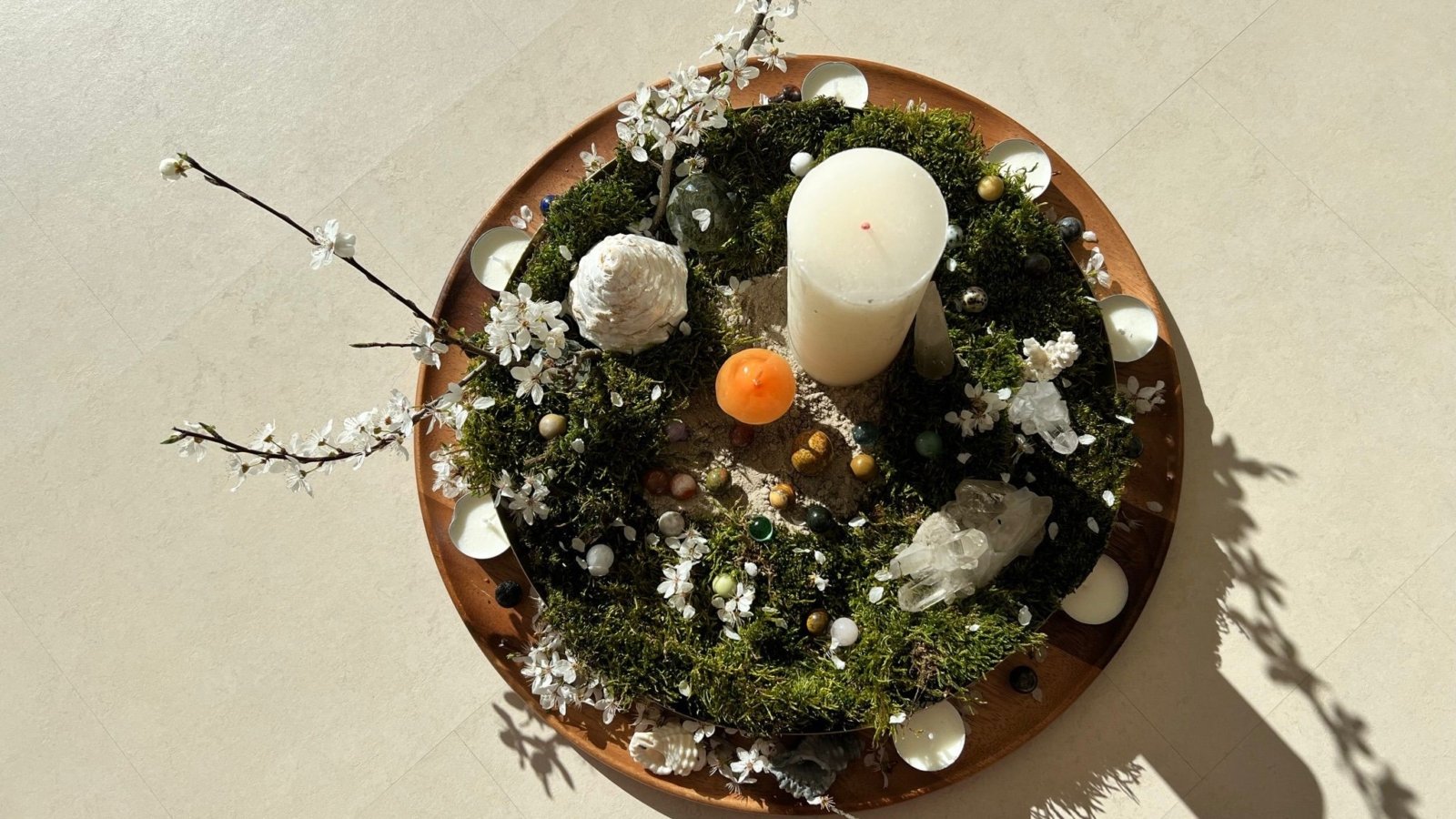 Centro de mesa redondo con musgo, velas, flores y piedras decorativas en una base de madera.