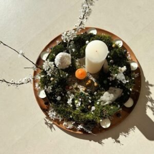 Centro de mesa redondo con musgo, velas, flores y piedras decorativas en una base de madera.