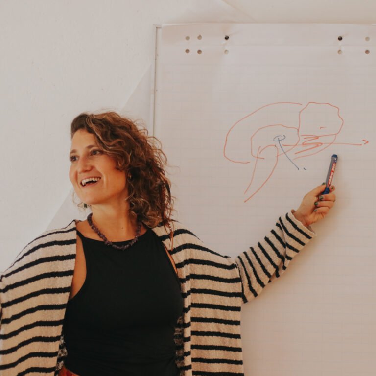 Woman with curly hair pointing at a diagram on a flip chart while holding a marker.