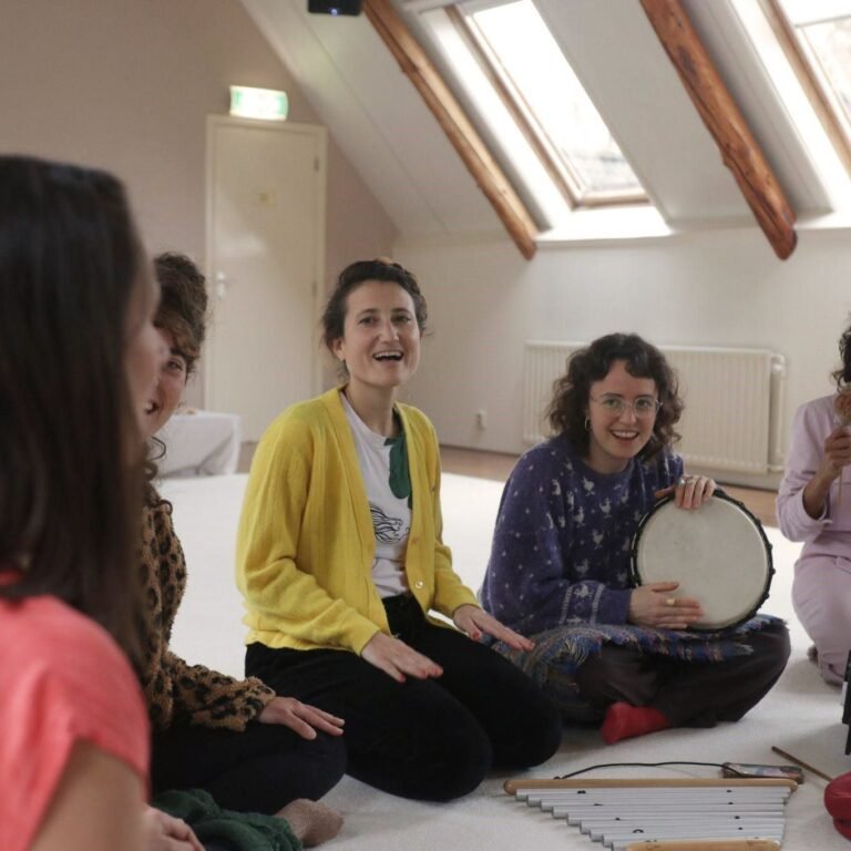 Cinco personas sentadas en un espacio interior, tocando instrumentos musicales y sonriendo.