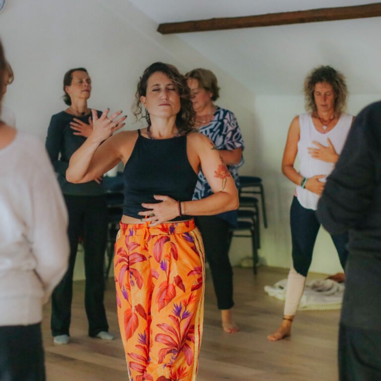 Group of women participating in a wellness exercise with hands on their chest in a bright room.